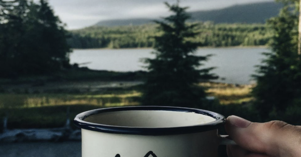coffee cup in foreground with mountains and lake