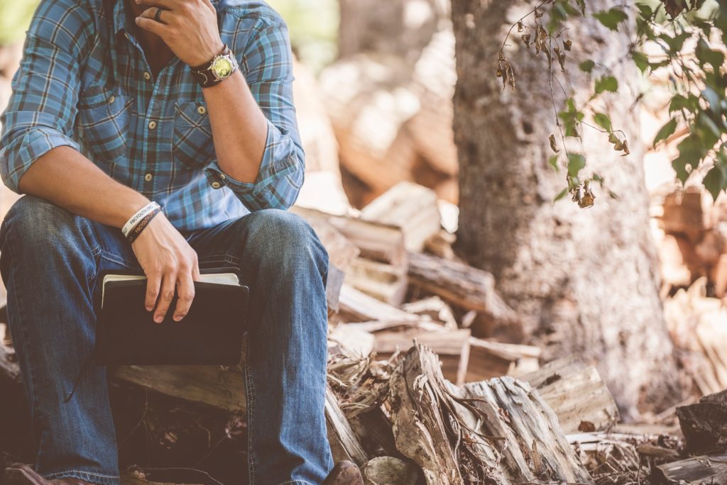 man sitting on wood pile with bible in his hand