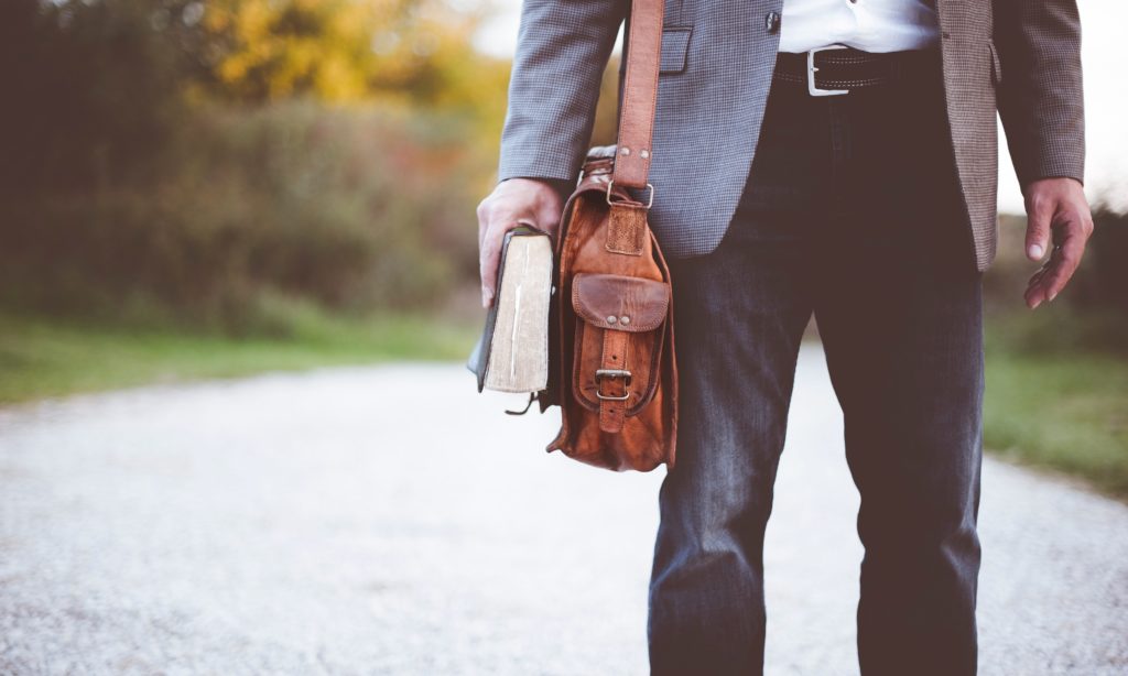 man holding book next to leather briefcase