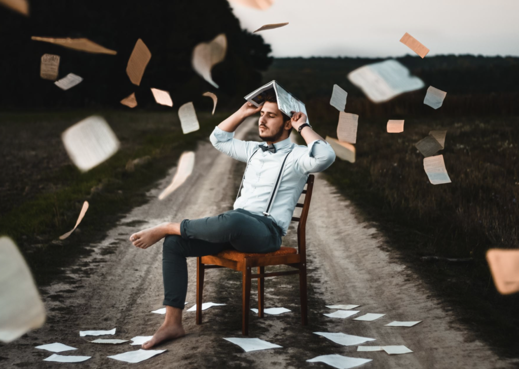 man sheltering his head with a book while papers fall all around him