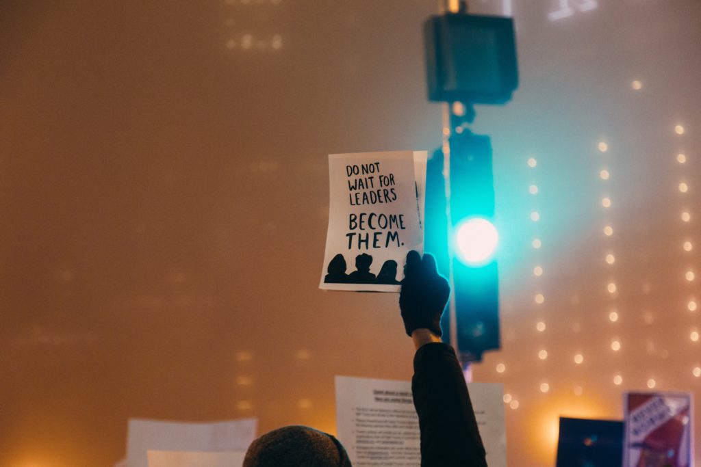 man holding sign that says do not wait for leaders become them